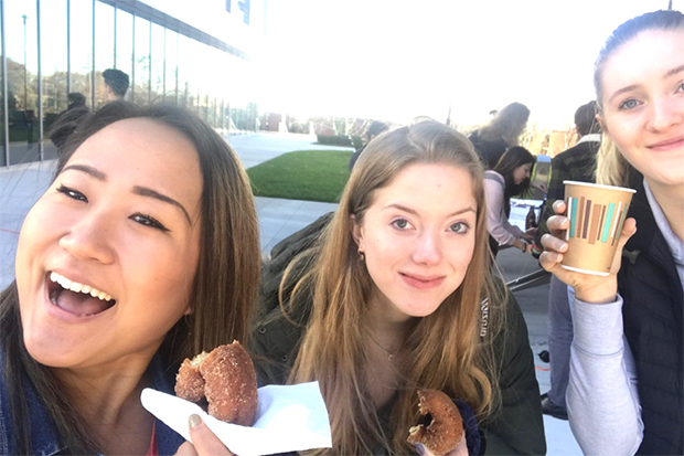 Cho takes a selfie with two other students. They are smiling and eating donuts.